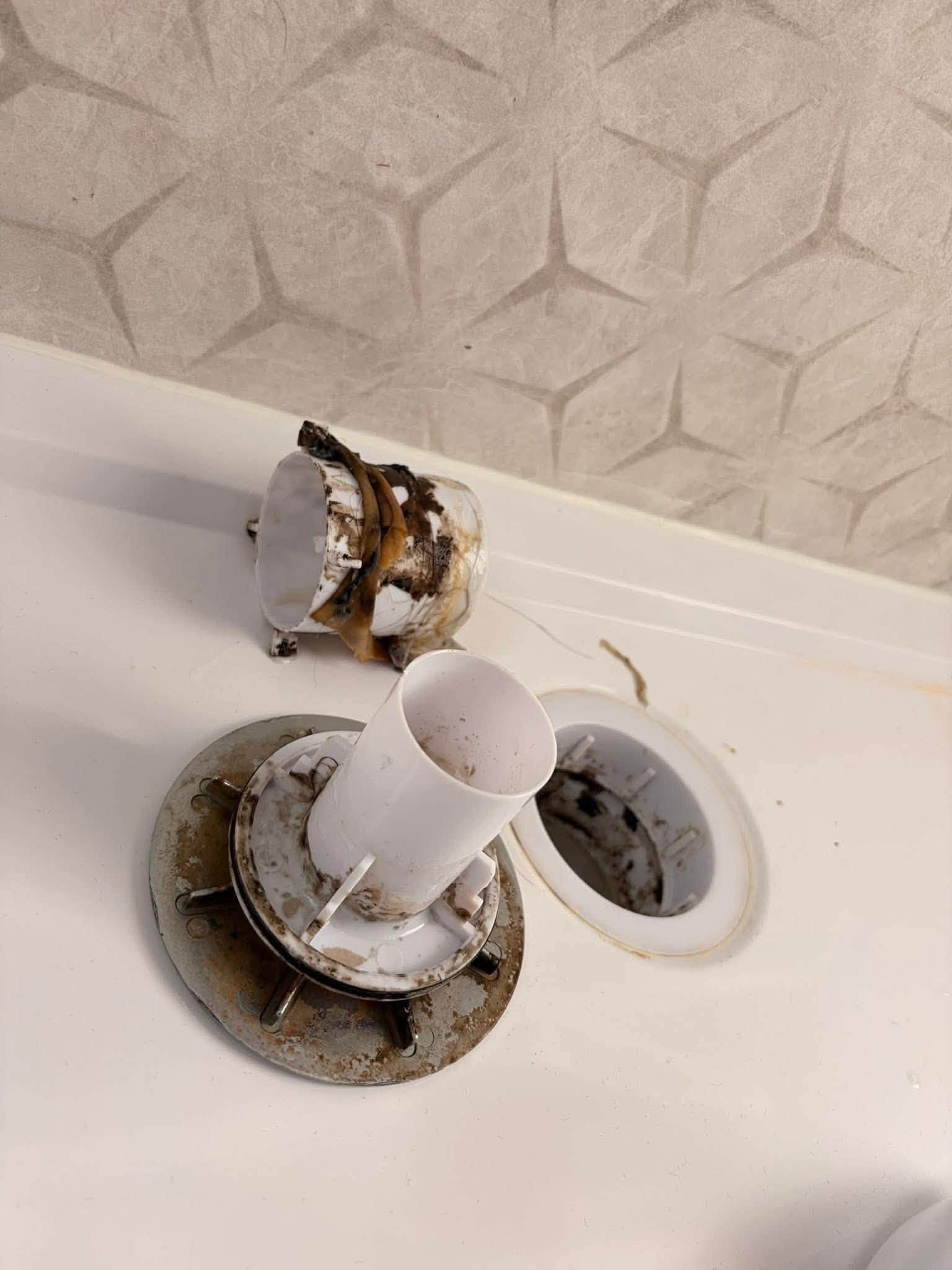 A dirty bath overflow and drain fitting caked in grime before cleaning