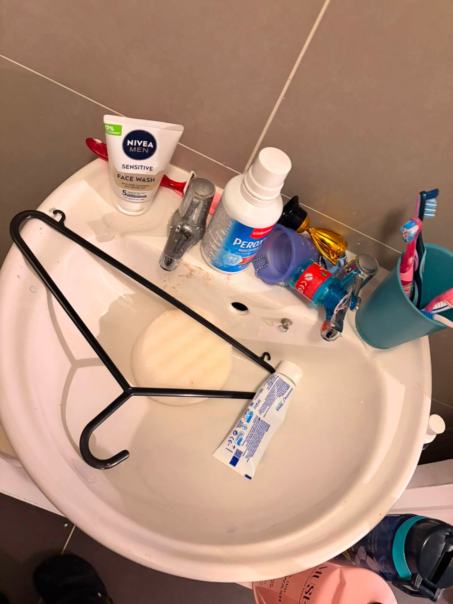 A cluttered, dirty bathroom sink before cleaning
